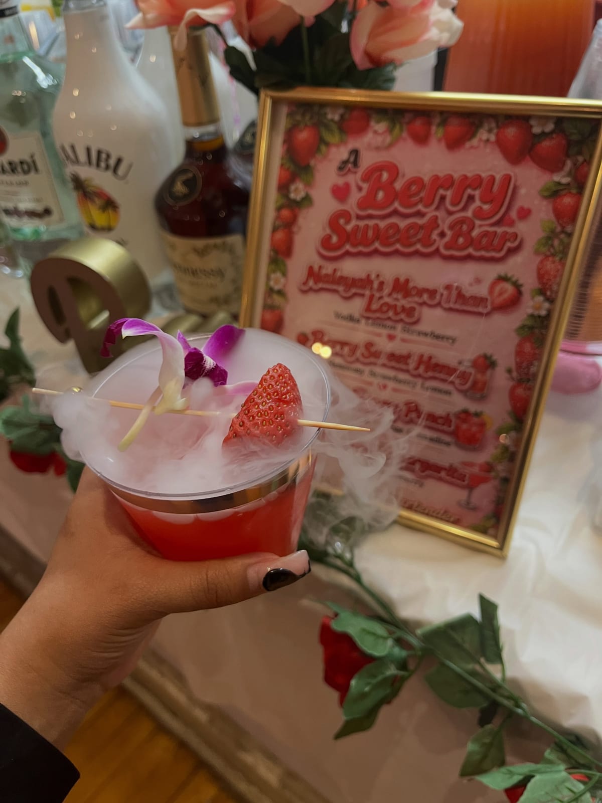 Smoking strawberry cocktail garnished with an orchid, held in front of a Berry Sweet Bar signature menu